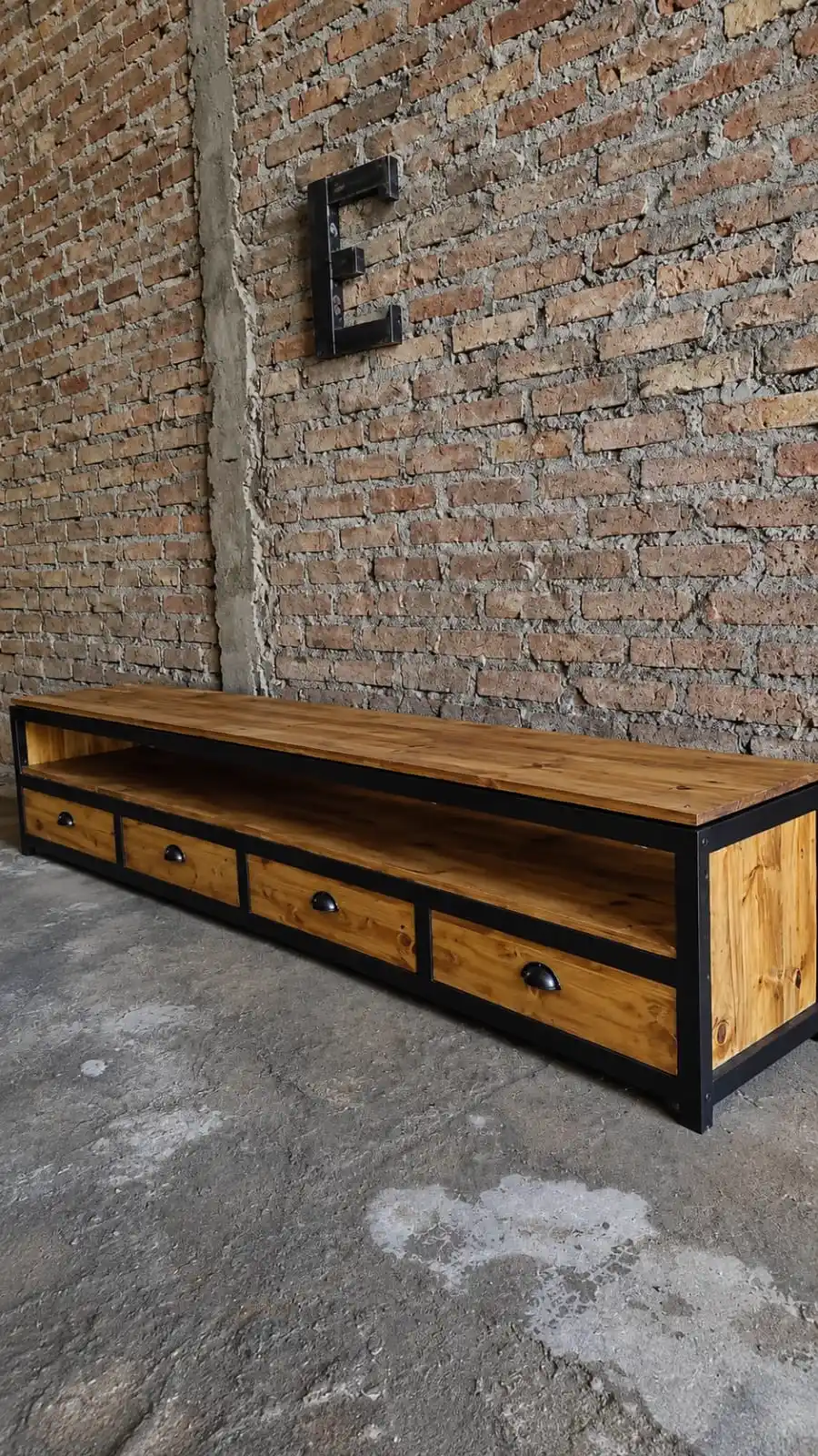 Bajo de TV industrial de hierro y madera con cuatro cajones, logo E metálico en pared de ladrillo