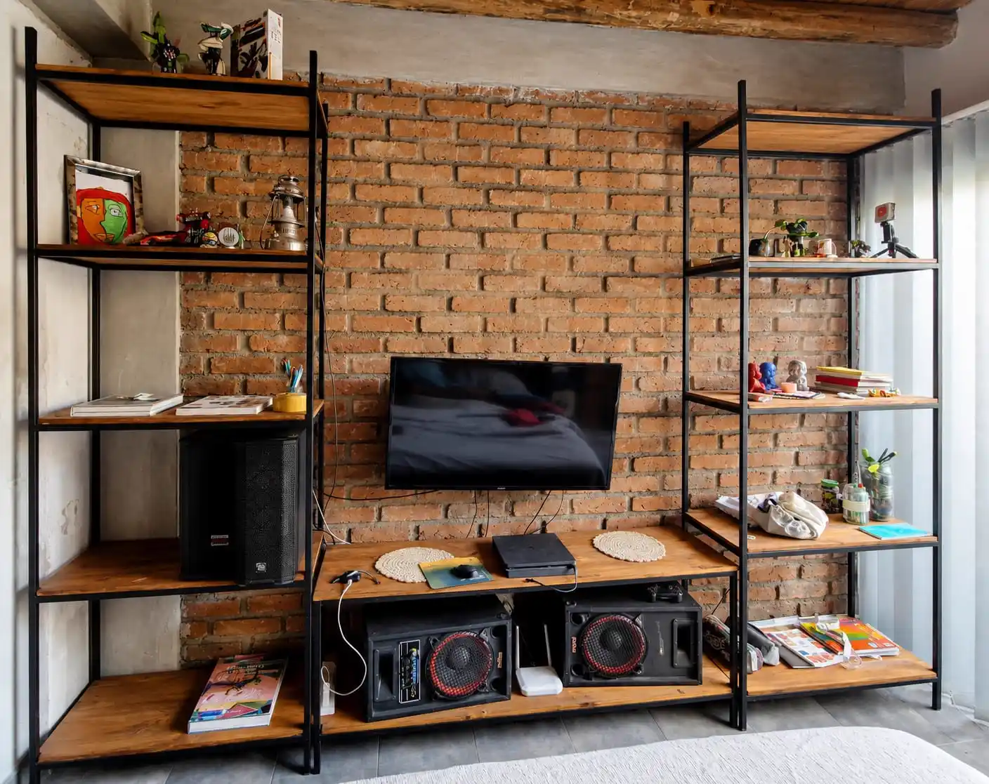 Estante industrial con TV al centro y estantes laterales con objetos, pared de ladrillo en living